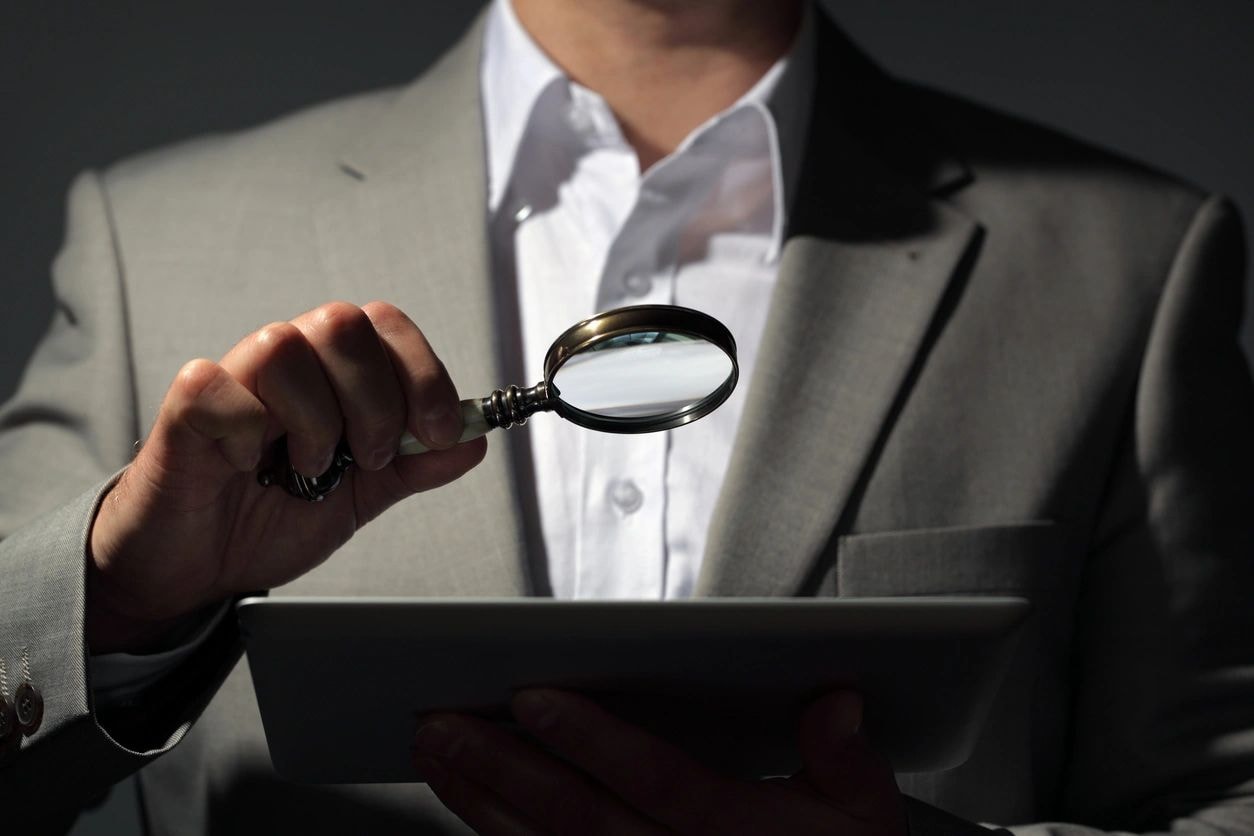 Professional investigator examining tablet with magnifying glass